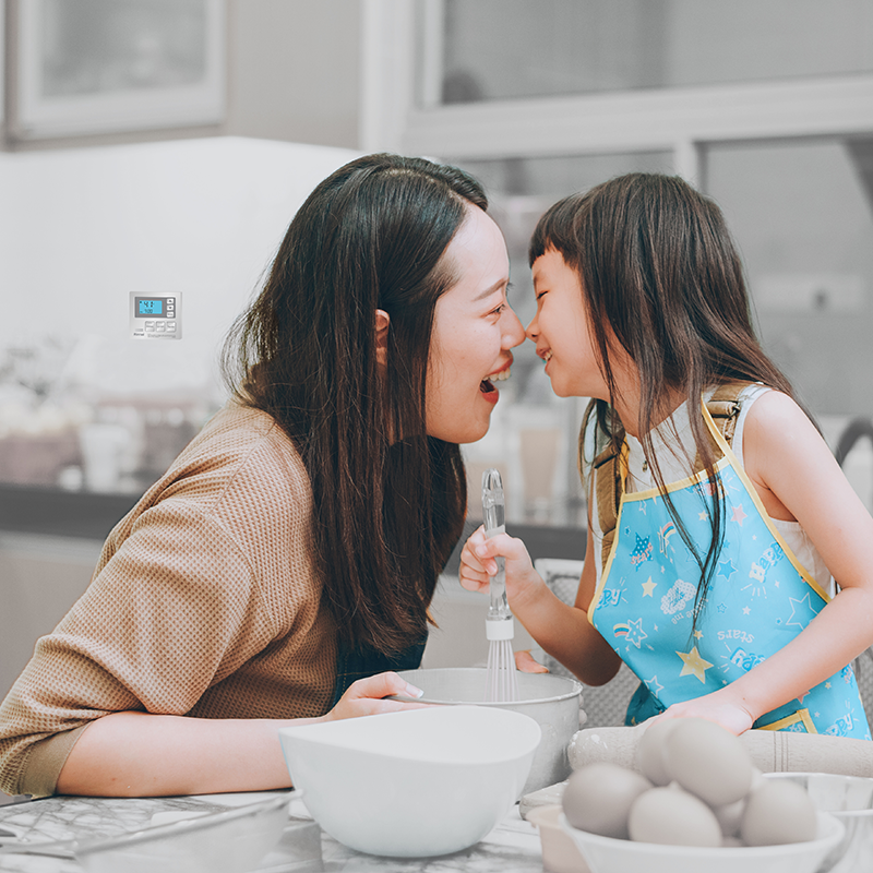 comando remoto Rinnai MC-100 ambientato in cucina con mamma e figlia giapponesi che sorridono mentre preparano una torta